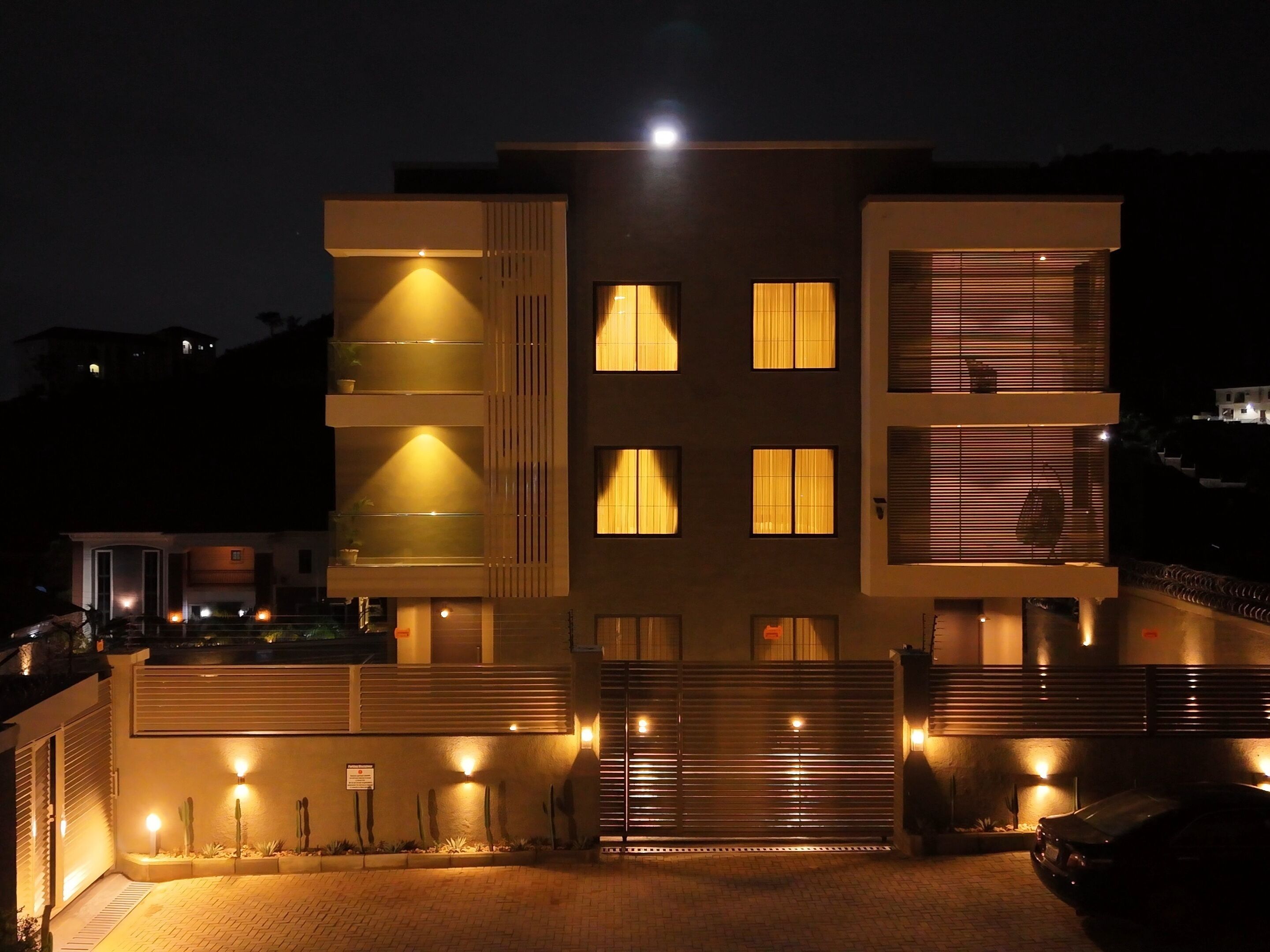A modern multi-story building with illuminated windows and a gated entrance.