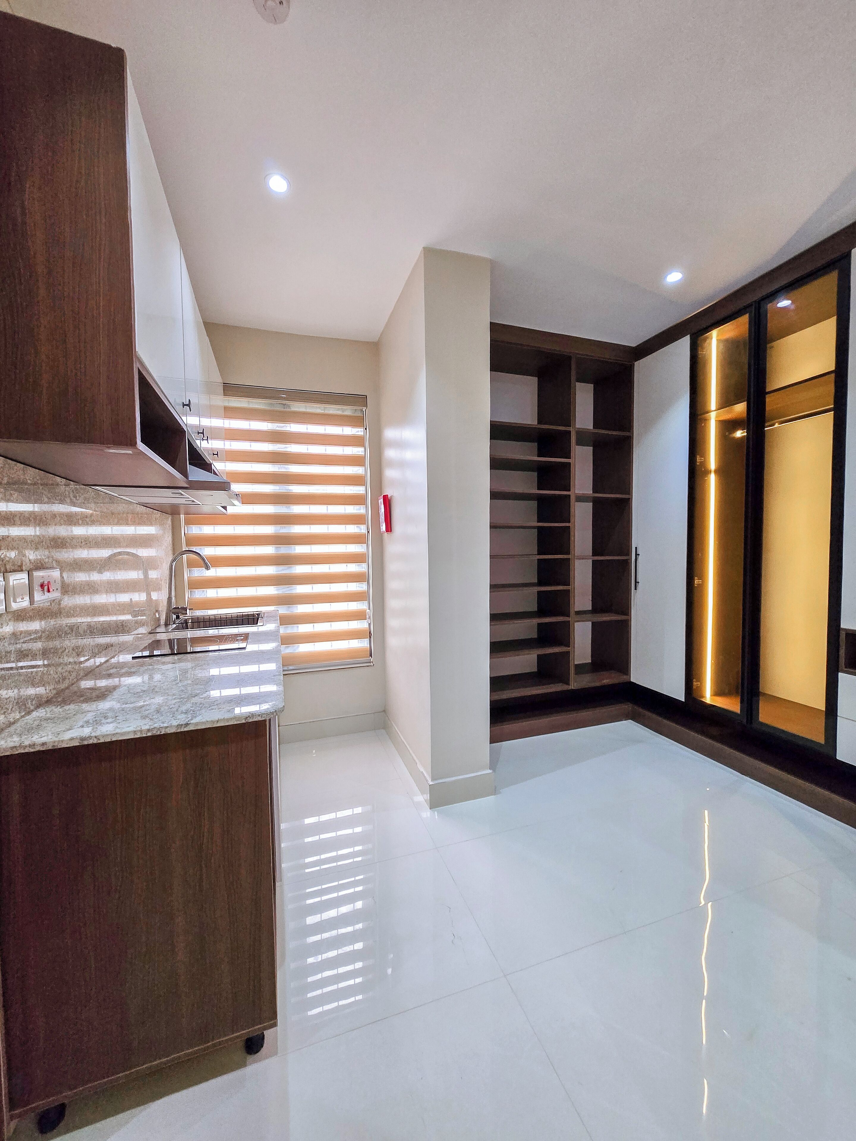 A modern kitchen with a marble countertop, wooden cabinets, and a built-in oven. There is a window with blinds and a sliding glass door leading to a closet.