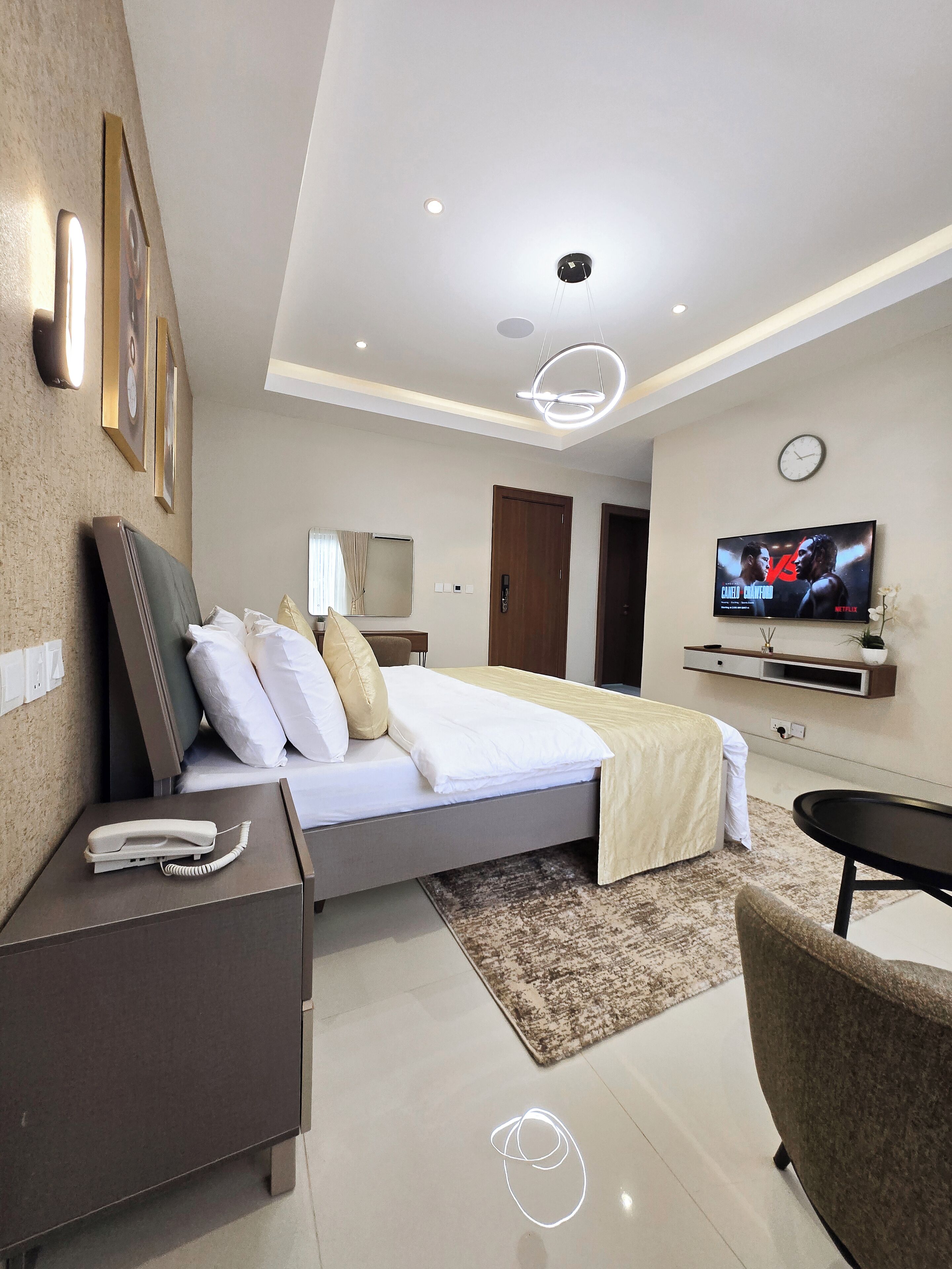 A modern hotel room with a neatly made bed, a bedside telephone, a television mounted on the wall, and a small table.