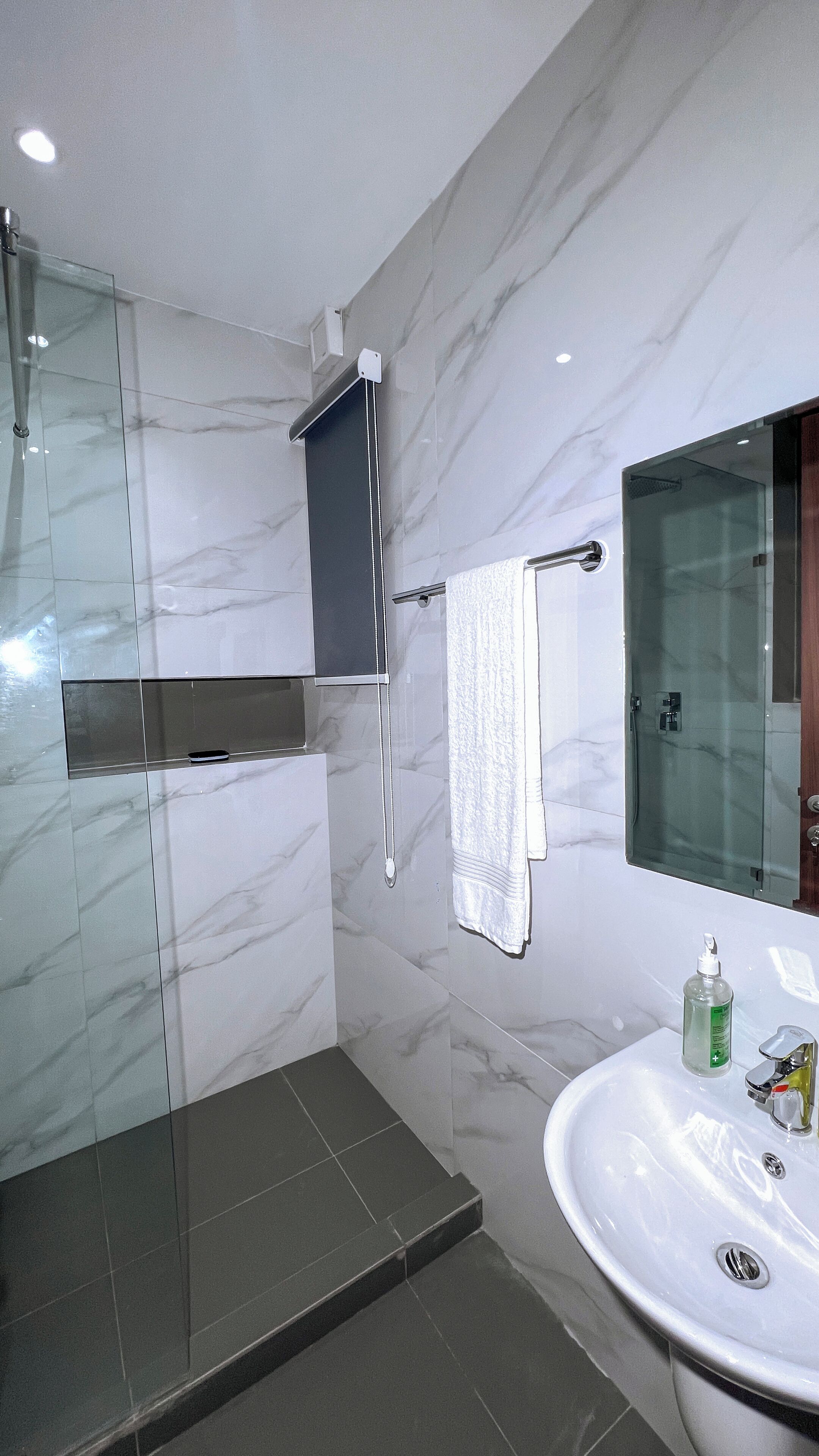 A modern bathroom with a glass shower enclosure, a marble-tiled wall, a built-in cabinet, and a sink with a mirror.