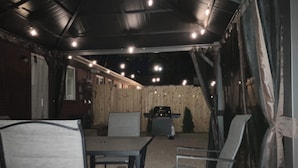 En udendørs patio med et bord, stole, grill og et træhegn.