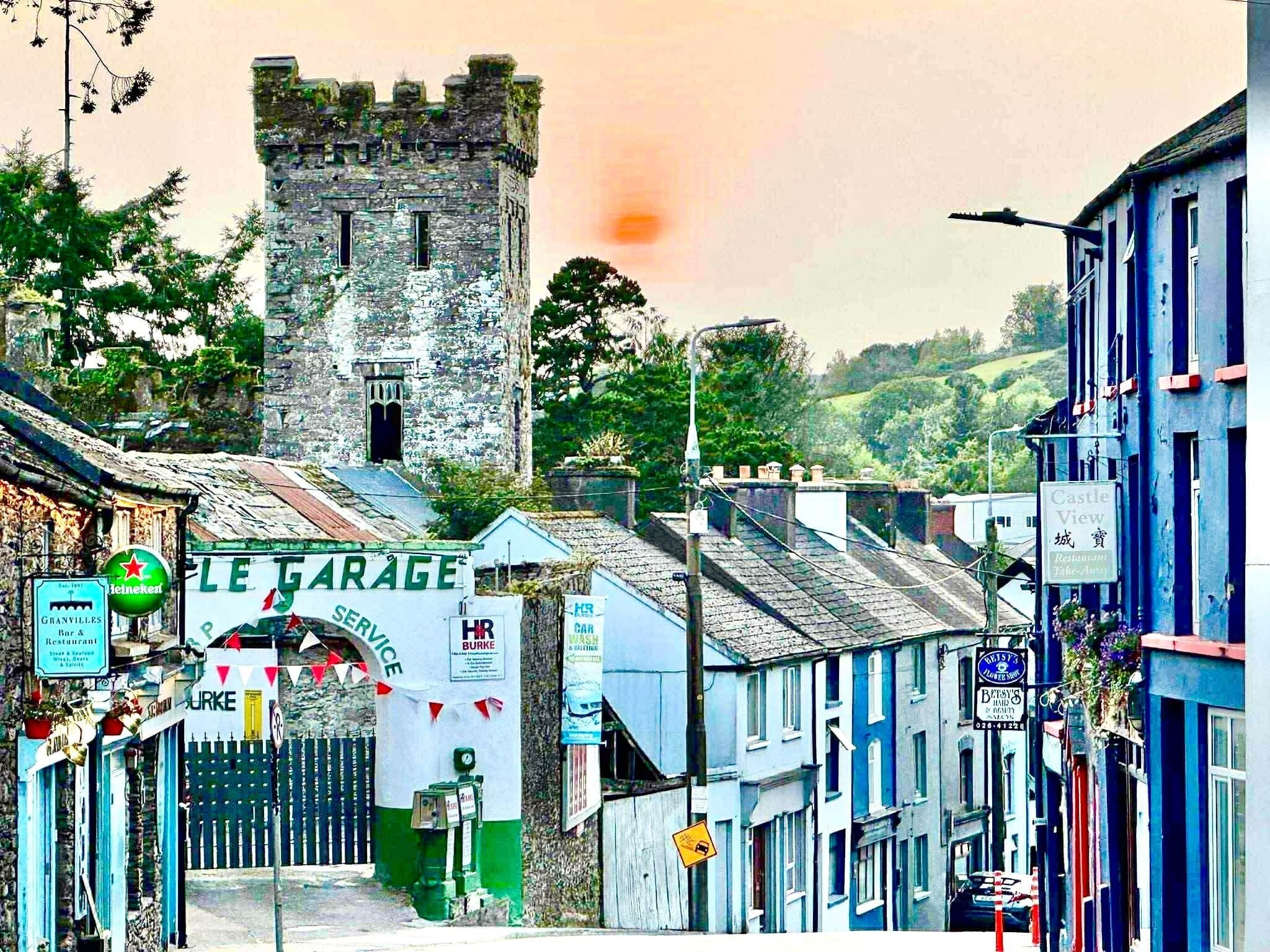A street with a castle in the background, a garage, and various shops.