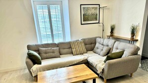 A living room with a grey sectional sofa, a wooden coffee table, a floor lamp, and a framed picture on the wall.