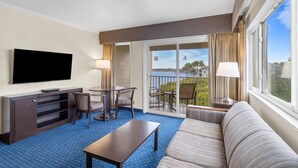 A hotel room with a flat-screen TV, a sofa, a coffee table, a dining table with chairs, and a balcony with a view of the ocean. - Bright & Convenient 2-Bed/2-Bath Condo (Tampa)