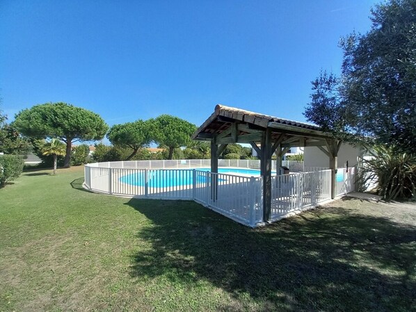 A fenced backyard with a pool, a covered patio, and a lawn.