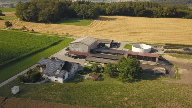 An aerial view of a farm with a large barn, solar panels, and surrounding fields.