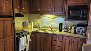A compact kitchen with wooden cabinets, a stove, a microwave, and a sink. - Welcoming RV with AC in charming Farmerville. (Farmerville)