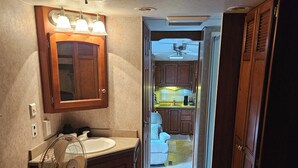 A compact RV interior with a kitchenette, a bathroom with a vanity, and a bed. - Welcoming RV with AC in charming Farmerville. (Farmerville)