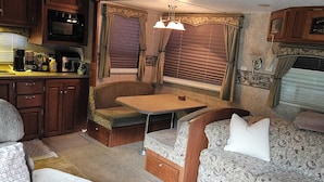 A compact RV interior with a kitchenette, a dining area, and seating. - Welcoming RV with AC in charming Farmerville. (Farmerville)