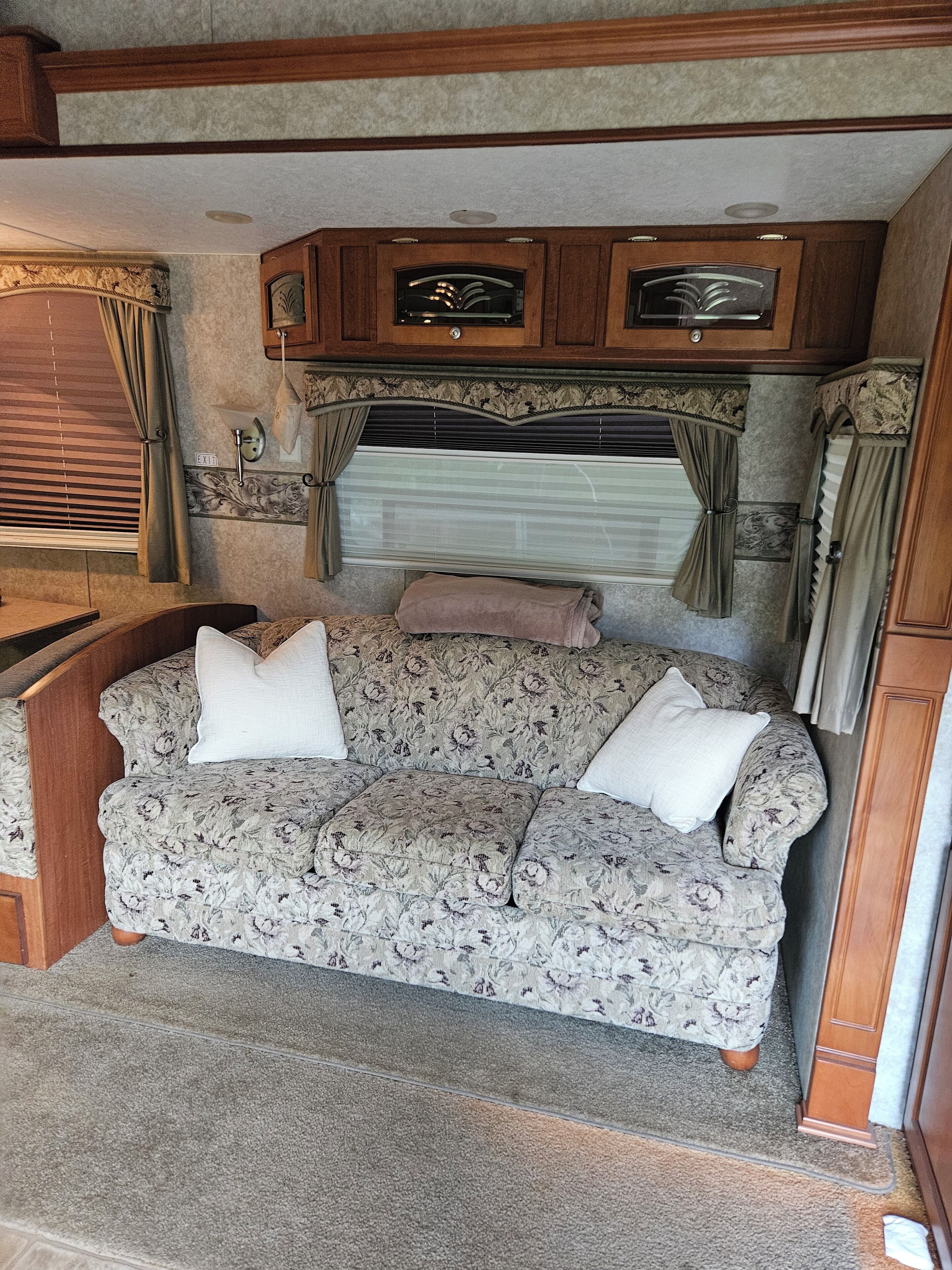 Een knus interieur van een camper, met een bank met bloemenprint, houten kastjes en een raam met gordijnen.