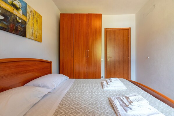 A bedroom with a wooden wardrobe, a bed with white linens, and a painting on the wall.