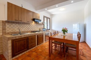 Une cuisine avec des meubles de rangement en bois, un plan de travail carrelé, un évier, une cuisinière et une table à manger avec des chaises.