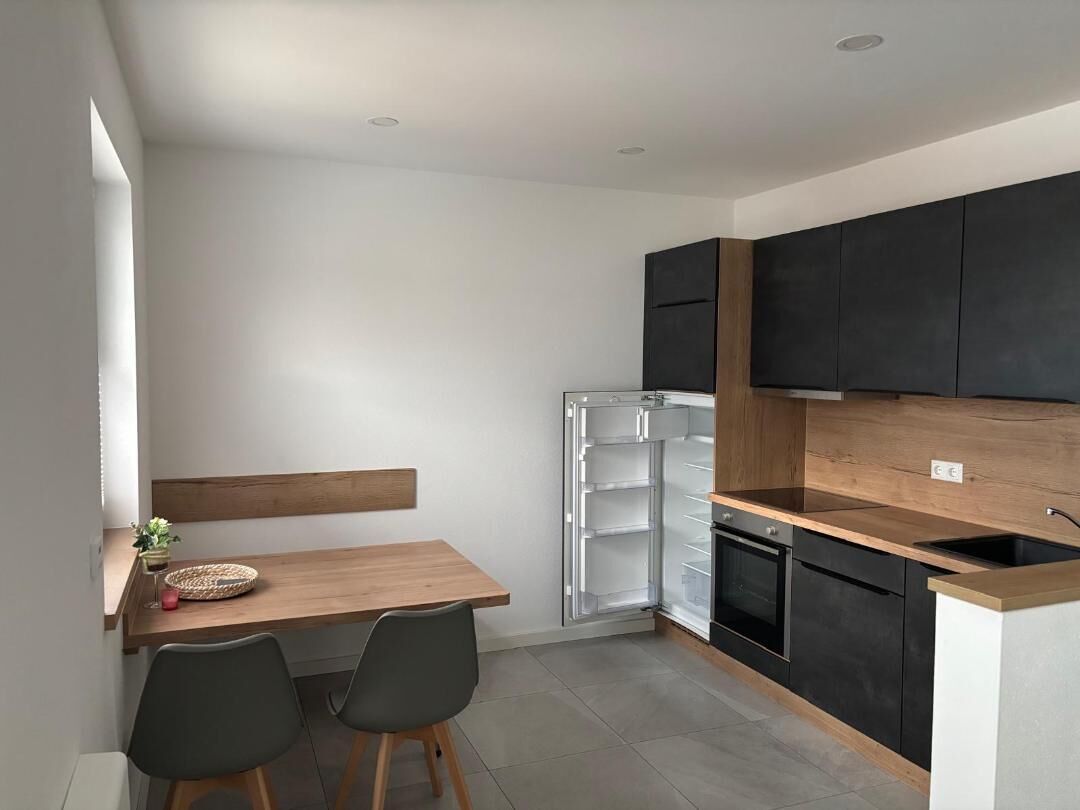 A compact kitchen with a wooden table and chairs, a built-in oven, and black cabinets.