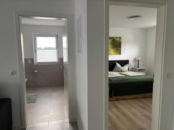 A bedroom with a bed, a nightstand, a lamp, and a painting on the wall. - New, modern 2-room apartment in Bad Füssing (Aigen am Inn) (Bad Füssing)
