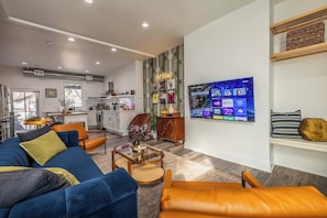 Uma sala de estar moderna com um sofá, cadeiras, uma mesa de centro e uma TV exibindo serviços de streaming.