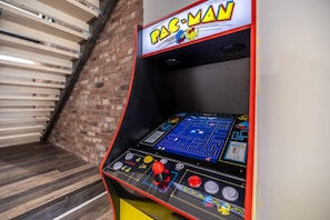 Máquina de arcade Pac-Man com joystick e botões, em frente a uma parede de tijolos e chão de madeira.