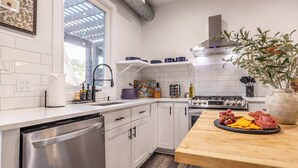 A modern kitchen with white cabinets, a stainless steel dishwasher, a built-in oven, and a wooden countertop with a charcuterie board.