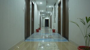 A hallway with a marble floor, potted plants, and doors on both sides. - Hotel Holiday Fun Resort (Kotputli)