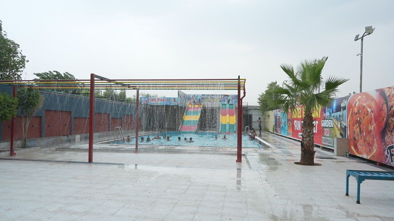 A swimming pool area with a water slide, surrounded by a tiled floor and a metal fence.