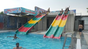 A swimming pool with two slides, a pool party sign, and a water park sign. - Hotel Holiday Fun Resort (Kotputli)
