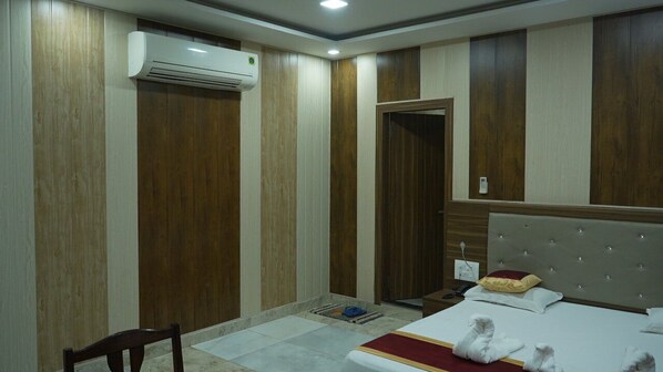 A hotel room with a bed, a chair, a wardrobe, and an air conditioning unit.