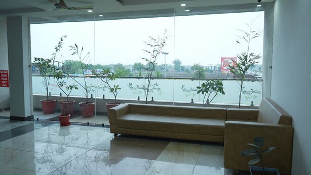 A reception area with a sofa, potted plants, and a view of a body of water. - Hotel Holiday Fun Resort (Kotputli)