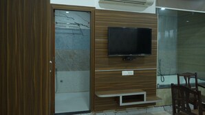 A room with a wooden wardrobe, a mounted TV, and a glass shower enclosure. - Hotel Holiday Fun Resort (Kotputli)