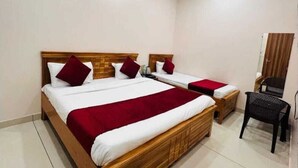 Habitación de hotel con dos camas de madera, cada una con ropa de cama blanca y detalles rojos, una mesita de noche pequeña, una silla negra y un armario de madera.