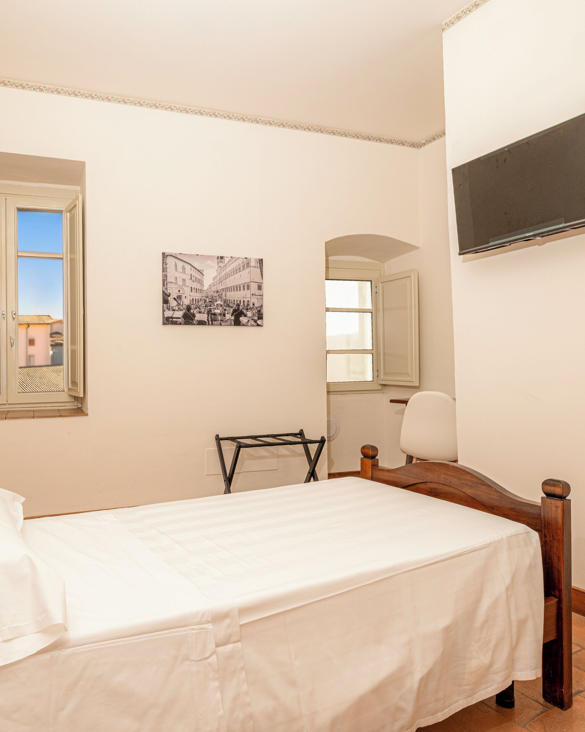 Quarto com uma cama, uma cadeira, uma televisão, uma janela e um quadro na parede.