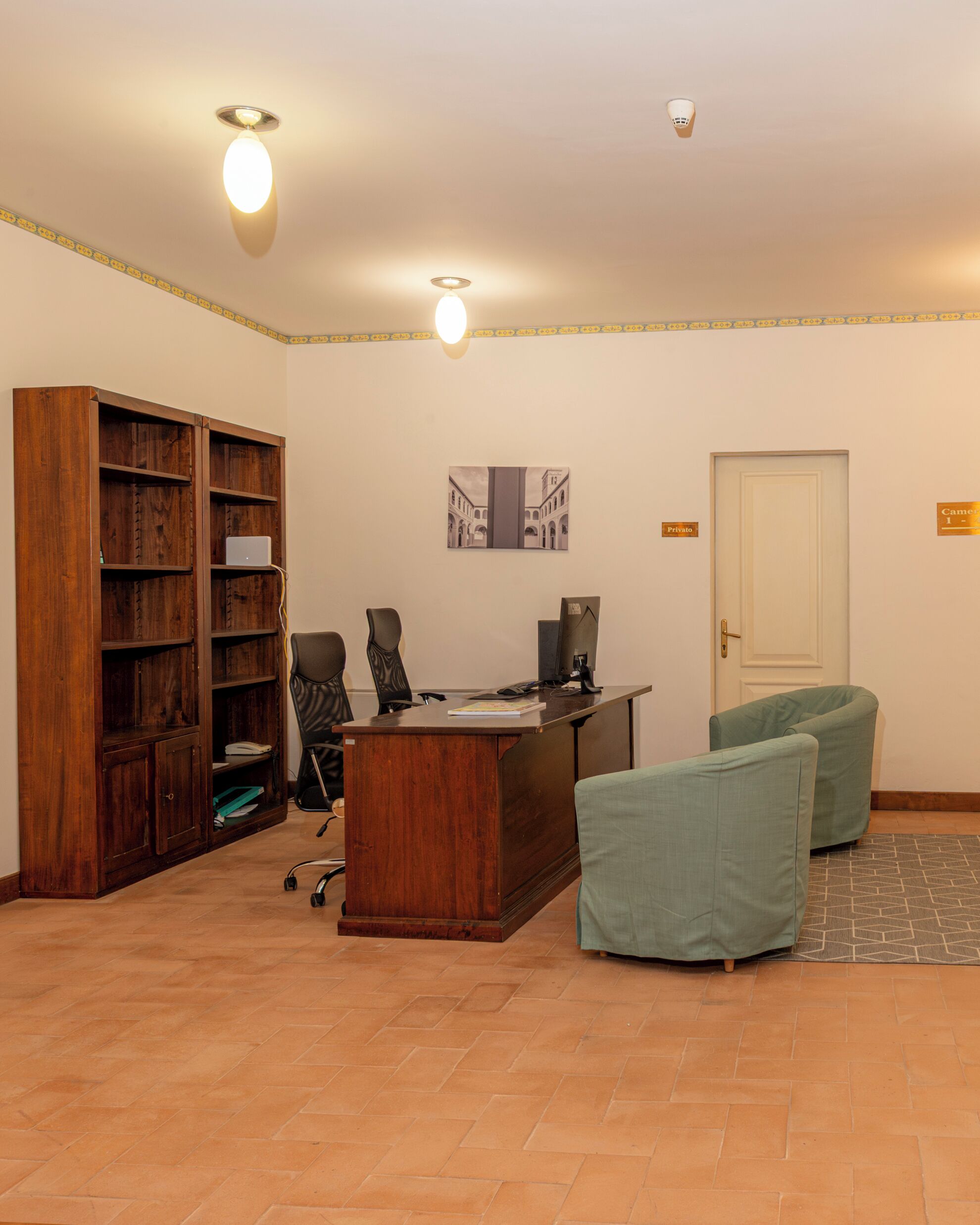 A room with a wooden desk, two chairs, a bookshelf, a door labeled "Private," and a wall-mounted picture.