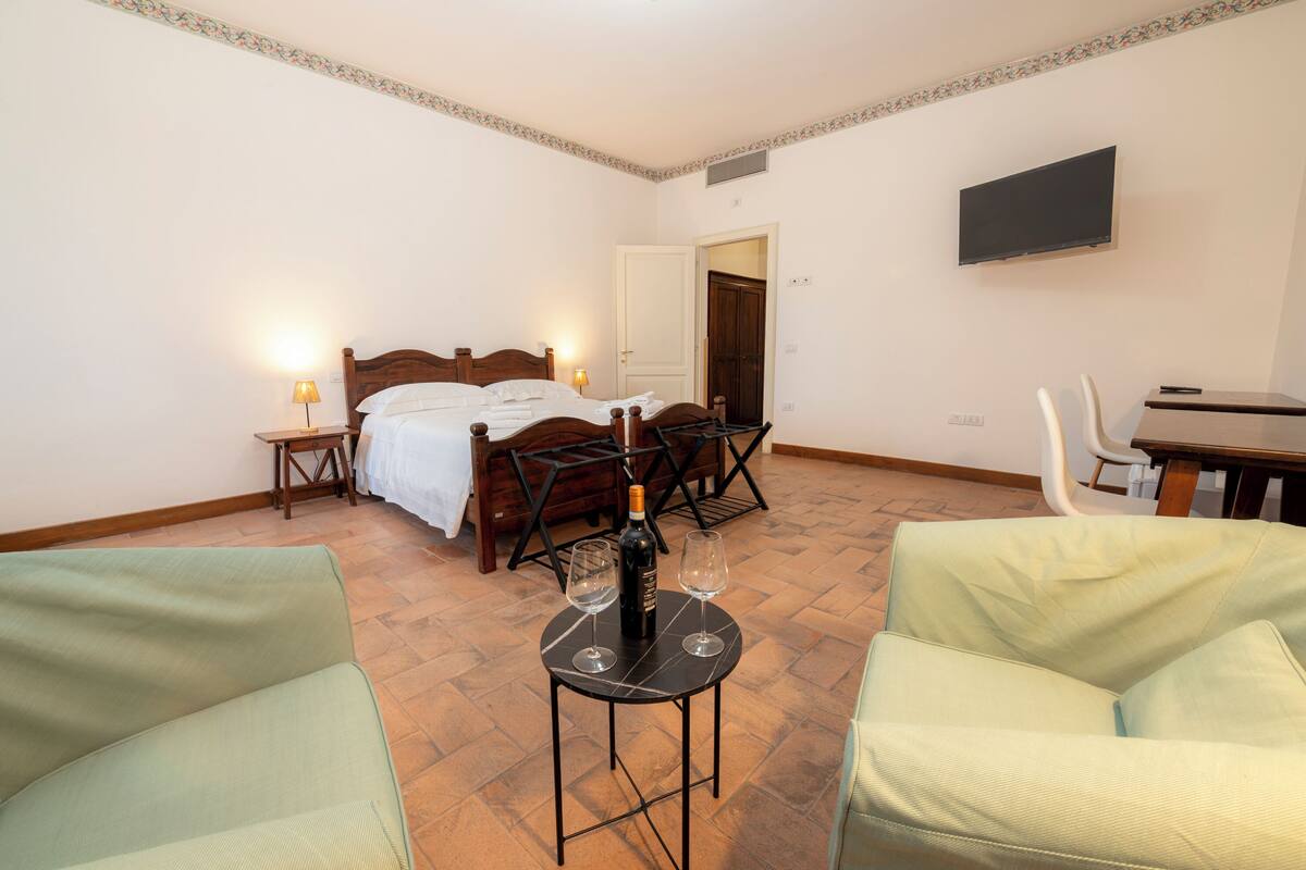 A hotel room with a bed, a desk, a TV, a small table with wine glasses, and two chairs.