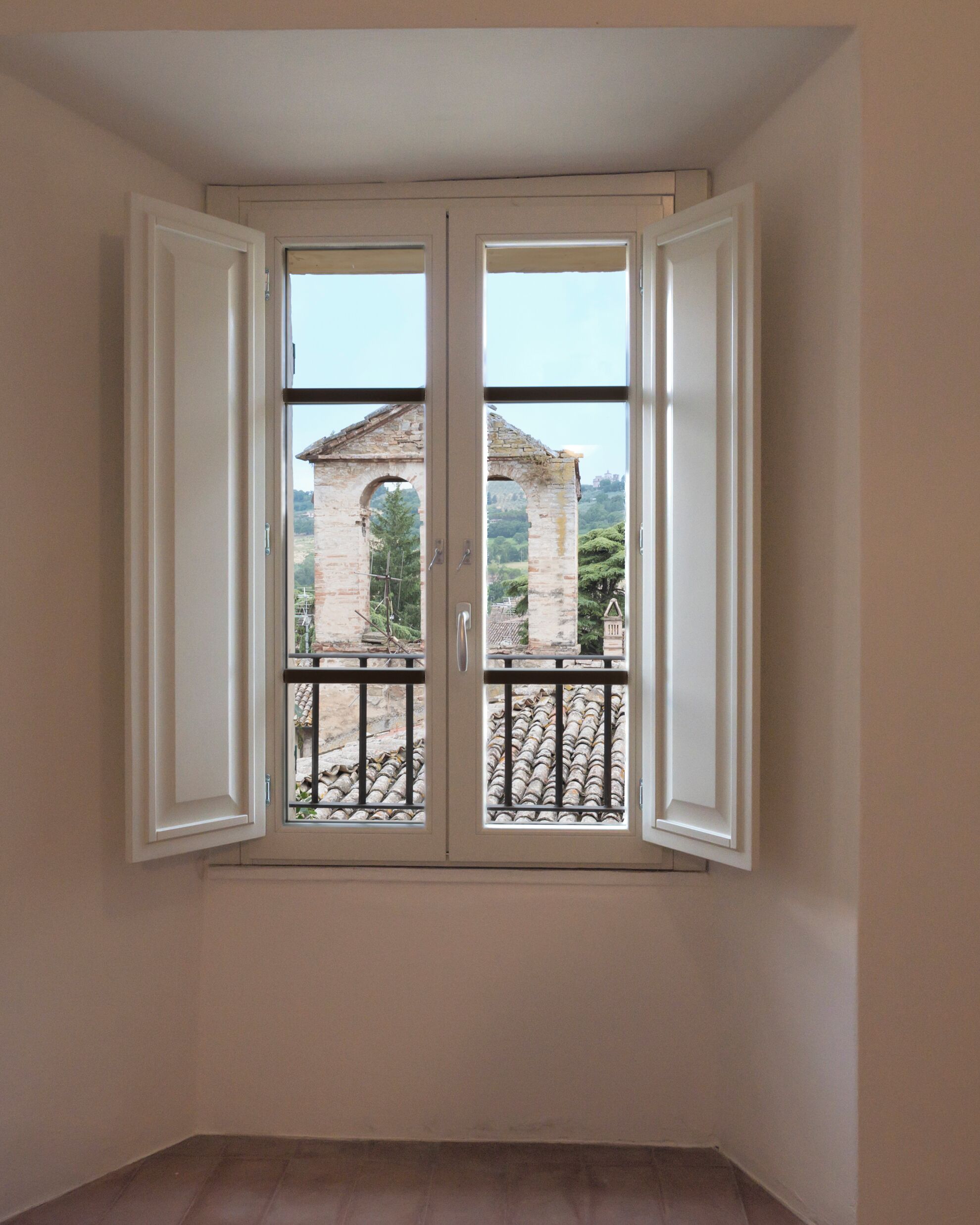 Una habitación con un ventanal que ofrece vistas a un edificio de piedra y un balcón de metal.