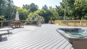 A wooden deck with a hot tub, outdoor furniture, and a view of trees.