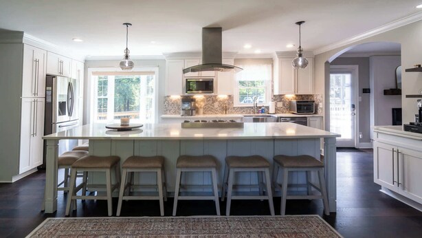 A modern kitchen with a large island, bar stools, and a patterned rug.