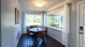 A dining area with a round table and chairs, large windows with curtains, and a door with a keypad lock.