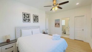 A bedroom with a bed, bedside tables, a ceiling fan, and artwork on the walls. - Coastal Beach House, Blocks from Ocean! (Myrtle Beach)