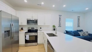 A modern kitchen with white cabinets, stainless steel appliances, and a large island. - Coastal Beach House, Blocks from Ocean! (Myrtle Beach)