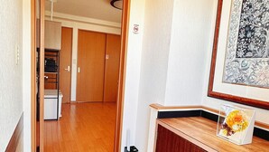 A hallway with wooden flooring, a set of wooden doors, a framed artwork on the wall, and a small wooden table with a vase. - HYGGE HOUSE Traveler's house (Kashiwa)