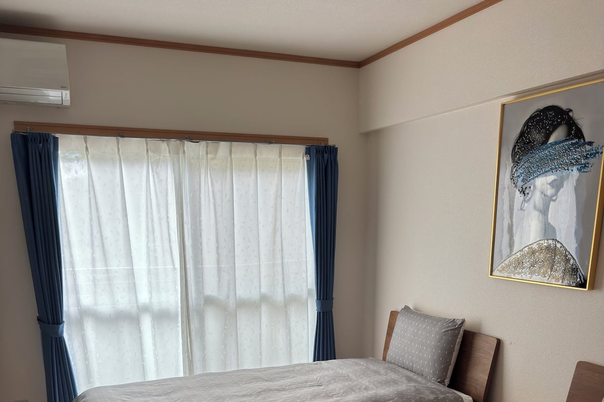 Une chambre d’hôtel avec deux lits, une table de chevet en bois, un tableau au mur et une fenêtre avec des rideaux.