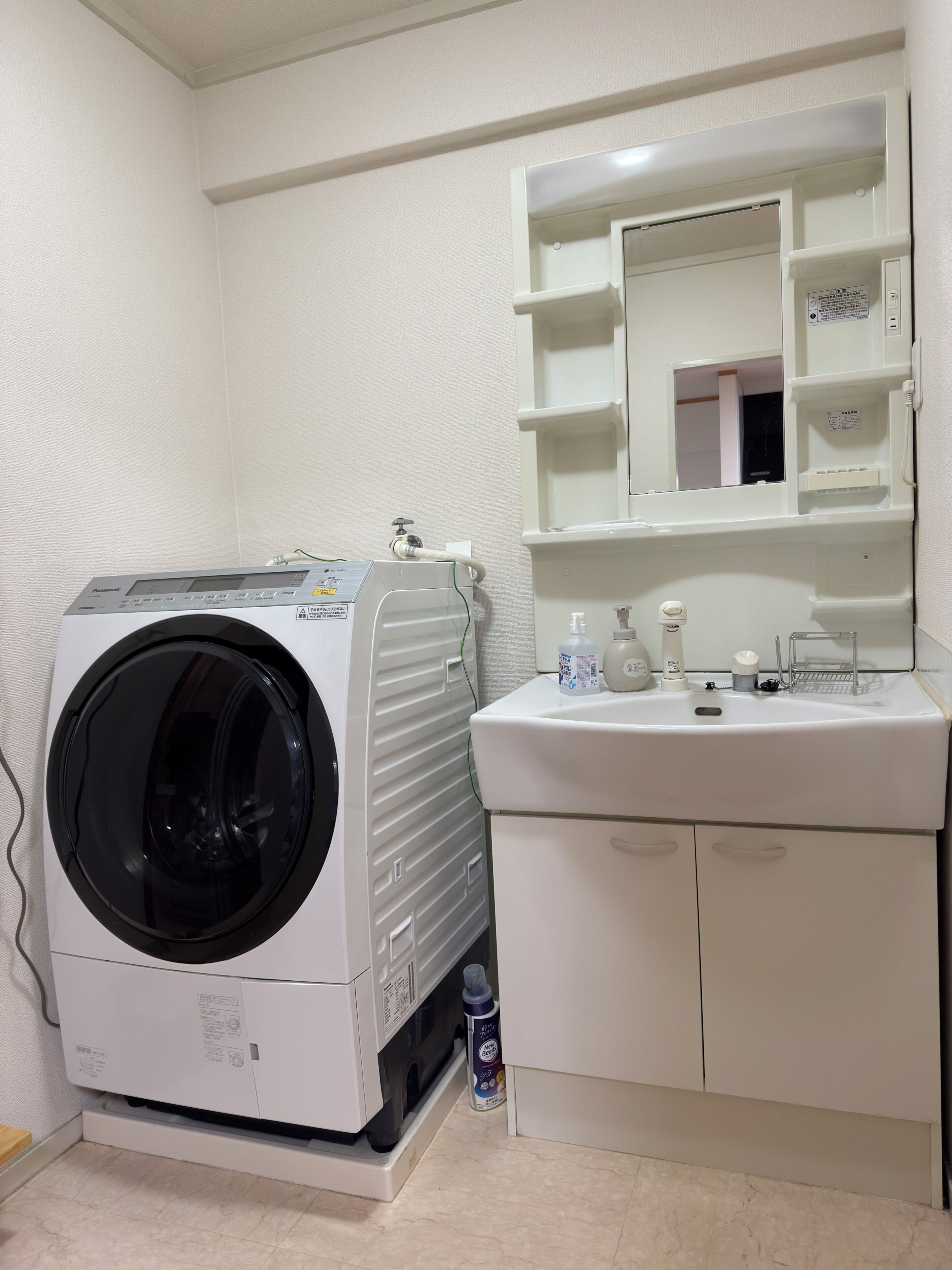 A compact laundry room with a front-loading washing machine, a sink with a mirror above it, and a small cabinet below.