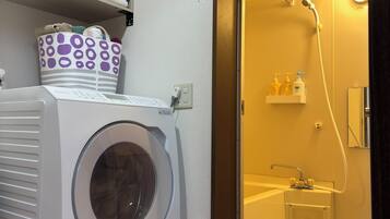 A laundry room with a front-loading washing machine, a drying rack, and a storage area with folded towels.