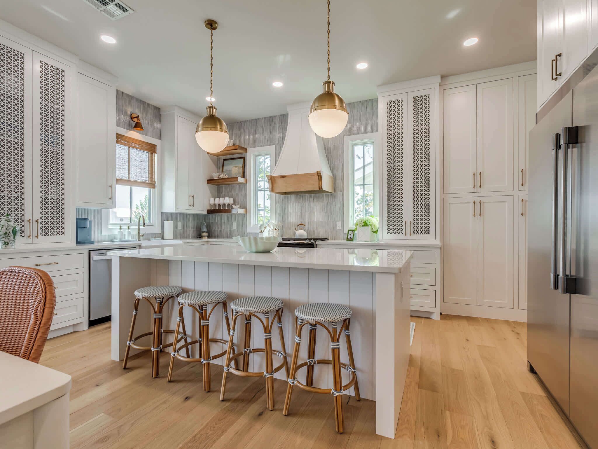 A modern kitchen with white cabinetry, a central island with bar stools, stainless steel appliances, and pendant lighting.