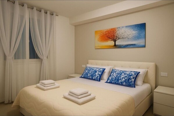 A neatly made bed with white linens and blue floral pillows, a painting of a tree on the wall, and a window with white curtains.