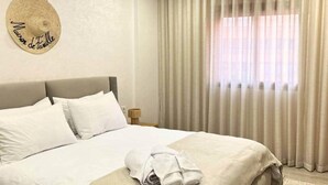 A neatly made bed with white linens, a round wall decoration, and a window with sheer curtains. - Sérénité Orientale I Apartment in Marrakech (Marrakesh)