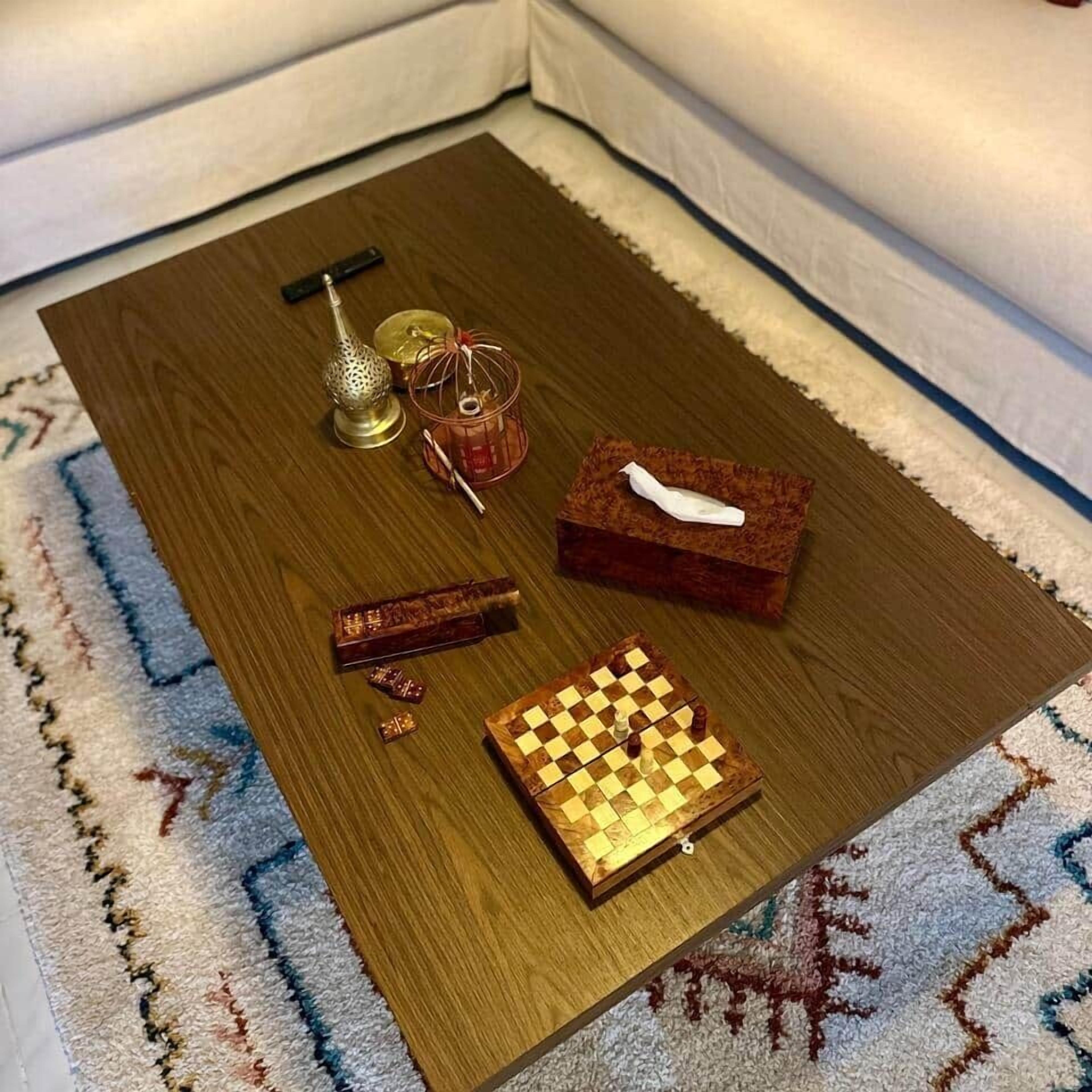 Une table basse en bois avec un jeu d’échecs, une petite cage à oiseaux, une lampe décorative et une boîte contenant un objet blanc.