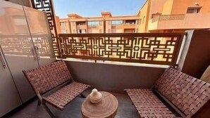 Un balcon avec deux fauteuils en osier et une petite table ronde.