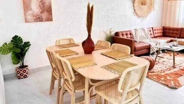 Un coin repas avec une table ronde en bois, six chaises et un vase central.