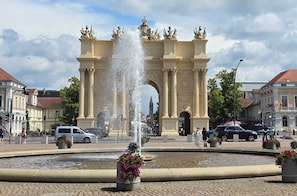 A historic archway with a fountain in the foreground, surrounded by cobblestone streets and buildings.