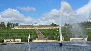 A large fountain with water jets, a grand building with classical architecture, and a well-maintained garden with a central staircase. - Apartment 'Am Park Sanssouci' (Potsdam)