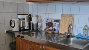 A kitchen with wooden cabinets, a stainless steel countertop, a coffee maker, a kettle, and a bottle of water. - Apartment 'Am Park Sanssouci' (Potsdam)